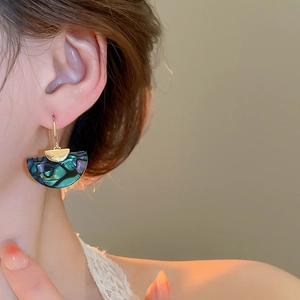 Close-up of fan-shaped earrings with iridescent abalone shell texture on female model