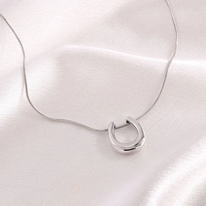 Detail of silver horseshoe pendant on white silk background with polished finish