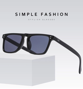 Detail view of square black sunglasses with silver rivet accents on a minimalist stone base