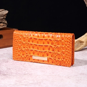 Detail view of amber orange crocodile pattern wallet with retro metallic accent on wood
