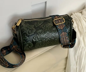 Detail of dark green vintage cylinder bag featuring 3D embossed leather and ethnic strap