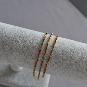 Close-up of three gold bracelets with colorful rectangle gemstones on a jewelry display