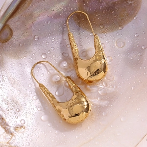 Détail de boucles d'oreilles en U plaquées or 18 carats sur une surface de nacre humide