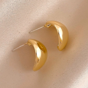 Macro shot of polished gold-tone geometric C-shaped hoop earrings on champagne satin