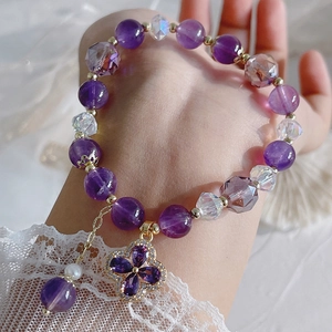 Detailed close-up of amethyst bead bracelet with clover charm and pearl on female wrist