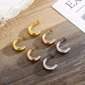 Minimalist C-shaped hoop earrings in gold, rose gold, and silver on a wooden surface