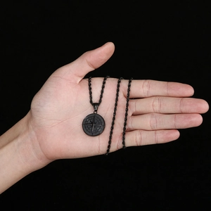 Gros plan d'un pendentif boussole noir sur chaîne torsadée tenu sur fond noir sombre