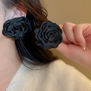 Close-up of elegant black satin camellia rose earrings worn by a female model