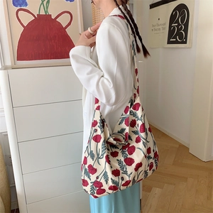 Side view of off-white canvas tote bag with red floral print worn in a modern room