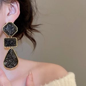 Detail of long geometric resin drop earrings in black and gold worn by a model