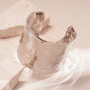 Close-up of silver wide open bangle with unique hammered texture on beige stone