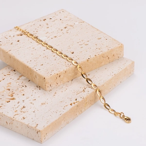 Gioielli a catena con maglie ovali dorate presentati su blocchi di pietra beige testurizzati
