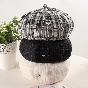 Close-up of stacked tweed berets in black and white plaid with heart-shaped metal buckles