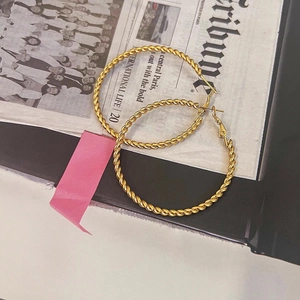 Detailed close-up of large golden twisted rope hoop earrings on a decorative background