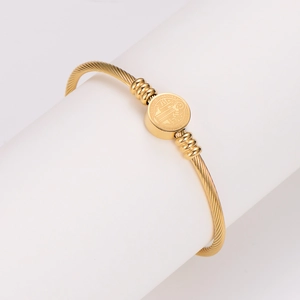 Golden twisted open bangle with round Saint Benedict medal on a white cylinder stand