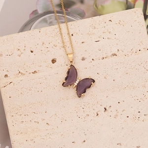 Vue détaillée du pendentif papillon violet avec chaîne dorée sur fond de pierre