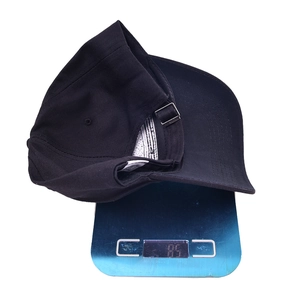 Detail showing the lightweight 85g black cotton baseball cap on a weighing scale