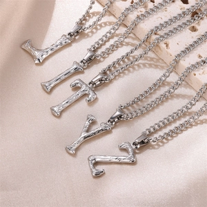 Detailed view of silver textured initial necklaces L I T Y Z on satin and travertine stone