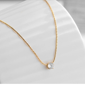 Macro shot of a six-prong zircon pendant on an 18K gold plated bamboo chain necklace