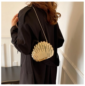 Detail of a golden shell-shaped acrylic evening bag with a metallic chain strap
