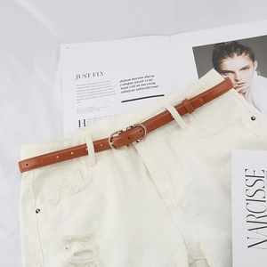 Thin brown leather belt with gold double-ring buckle styled on white jeans with magazine