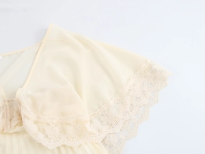 Dettaglio di eleganti pizzi beige e volant in chiffon plissettato su un abito romantico