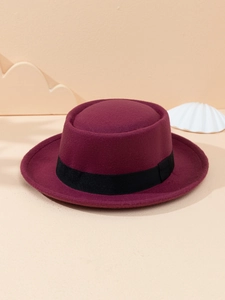 Detail of burgundy wool felt flat top hat with black ribbon on warm backdrop