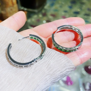 Detailed close-up of emerald green stones set in silver hoop earrings held by a hand