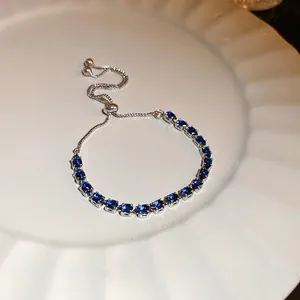 Adjustable silver bracelet with blue teardrop cubic zirconia on a white ceramic plate