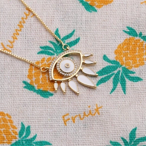 Detail of gold evil eye pendant with micro-pave crystals and white enamel teardrops