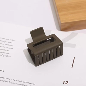 Detail view of square matte olive green hair claw clip with cutout design on wood