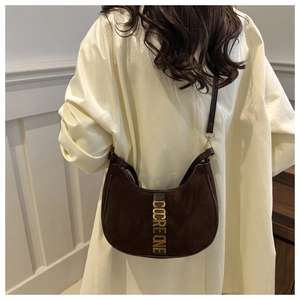 Detail of dark brown suede crescent bag with gold metal logo worn over the shoulder