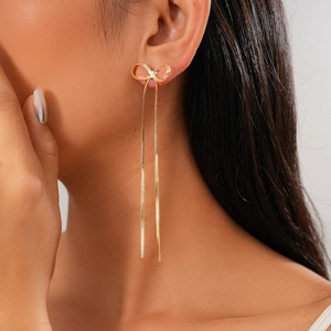 Detail shot of elegant gold bow earrings with long tassels on female model side profile