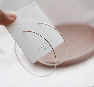 Minimalist large silver metal hoop earring displayed on a white branded back card