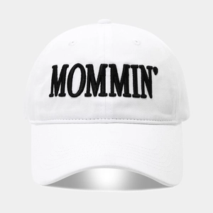 Close-up of MOMMIN' black letter embroidery on the front of a white cotton baseball cap