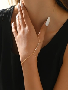 Close-up of a gold hand chain with delicate pearls connecting a ring and bracelet
