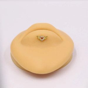 Close-up of golden heart labret stud with wings and crystals on a silicone display model