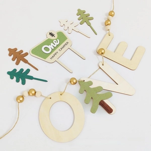 Detail of wooden One Happy Camper birthday cake toppers and green pine tree party decorations