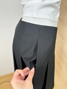 Detail shot of a black pleated skirt featuring a hidden side pocket and twill texture