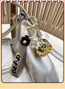 Détail d'un porte-clés panda avec paillettes liquides suspendu sur un sac argenté