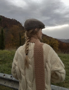 Detailed texture of chunky cable knit sweater paired with a stylish brown checkered cap
