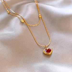 Close-up of double-layered gold necklace with red heart pendant on champagne silk fabric