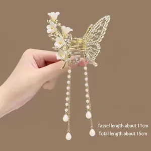Detail of golden metal butterfly hair claw with white flowers and long pearl tassels