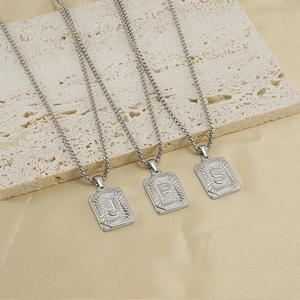 Close-up of square silver stainless steel initial pendants with radial texture details