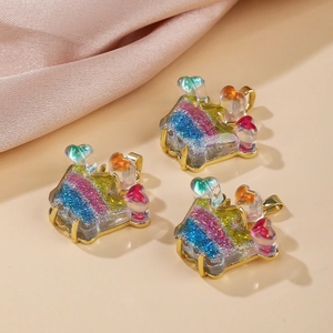 Three glittering rainbow house resin charms with gold metal frames on beige fabric