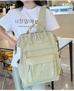 Close-up of light green nylon backpack featuring cute bear embroidery and multi-pocket design