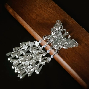 Detail of silver butterfly hair clip with metallic tassels on a vintage wooden base