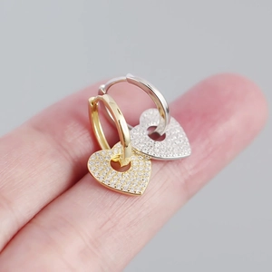 Macro shot of silver heart hoop earrings with pavé zircons held by a hand