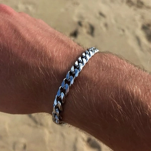 Close-up of silver Cuban link chain bracelet on wrist with a beach background