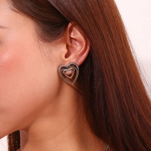 Detail showing a silver-finished double-layered hollow heart stud earring on a model